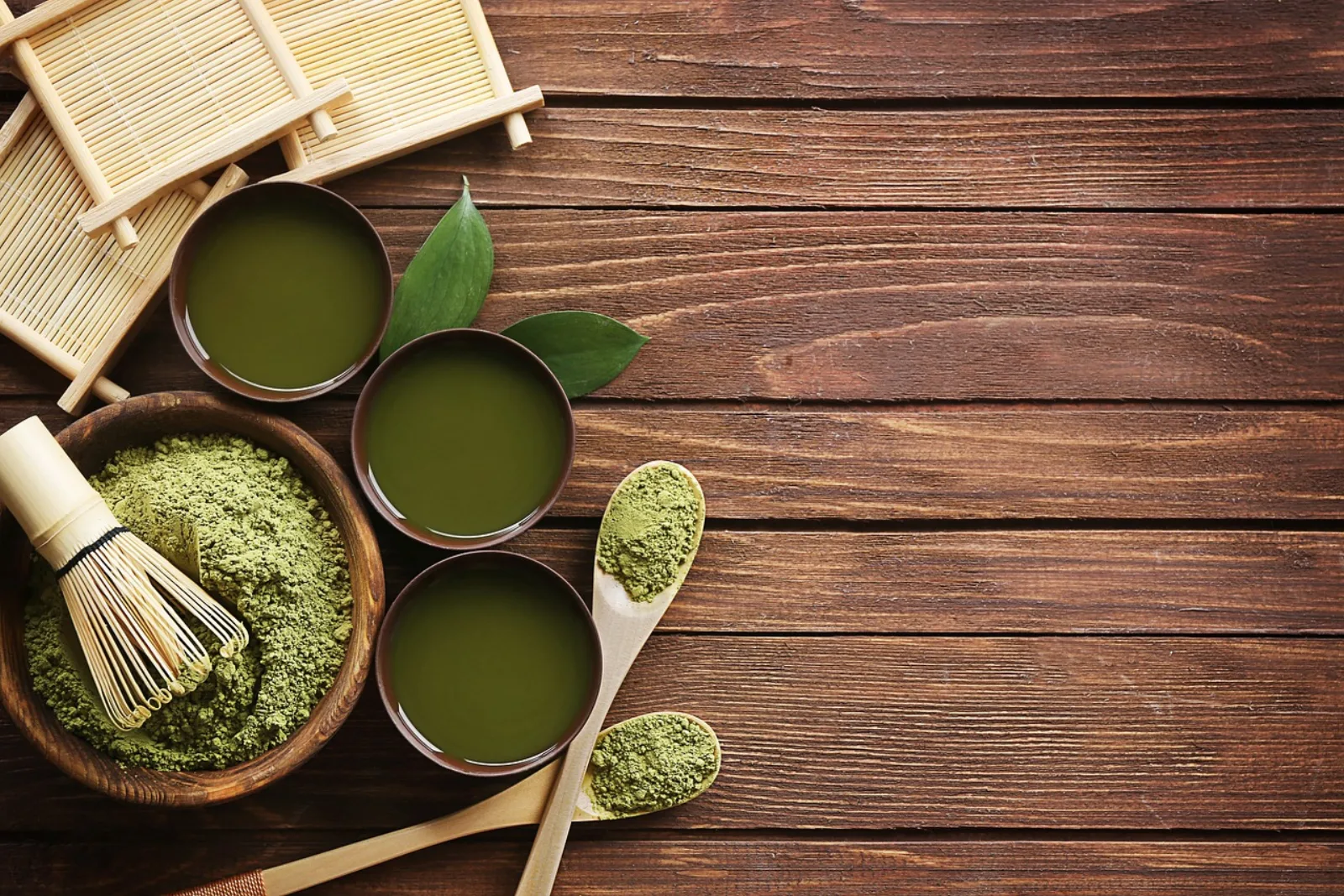 Poudre de matcha vert vif dans un bol, à côté d'une cuillère en bambou